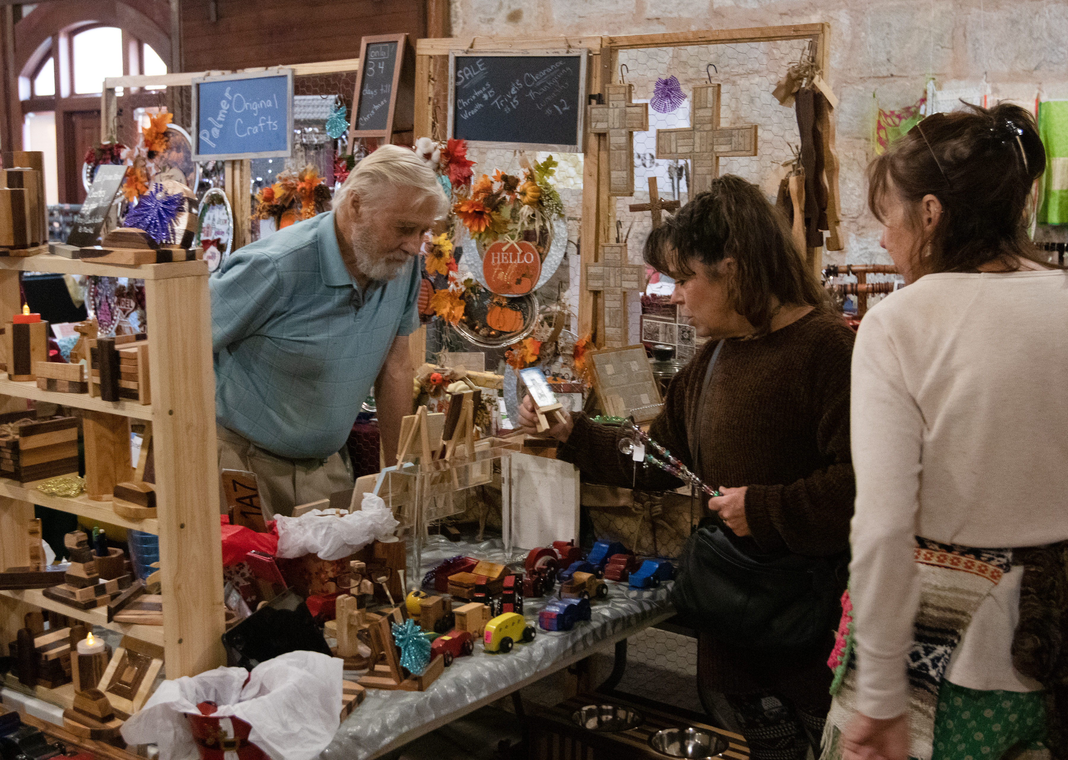 Gary Palmer talks with visitors at the Christmas Market in Crawford on Nov. 21. Palmer makes wooden toys and other items by hand and sells them with his wife, Naomi Palmer, who also handmakes decorations and items. (Photo/Sarah White)