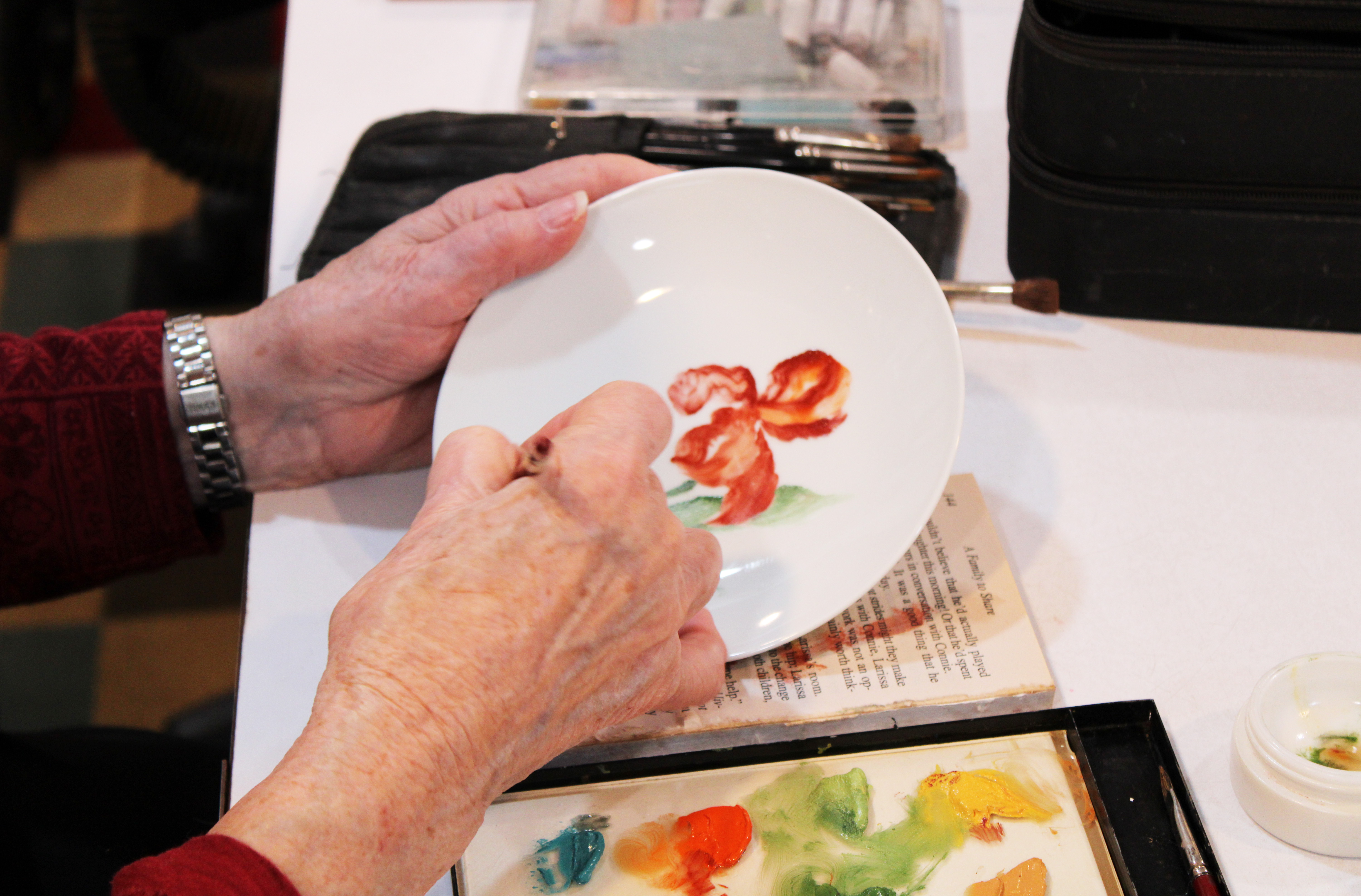 Jane Bowen paints a flower on a plate in her studio in Crawford.  She also paints lamps, furnishings, tiles and dishes. (Shannon Moran/The Oglethorpe Echo)