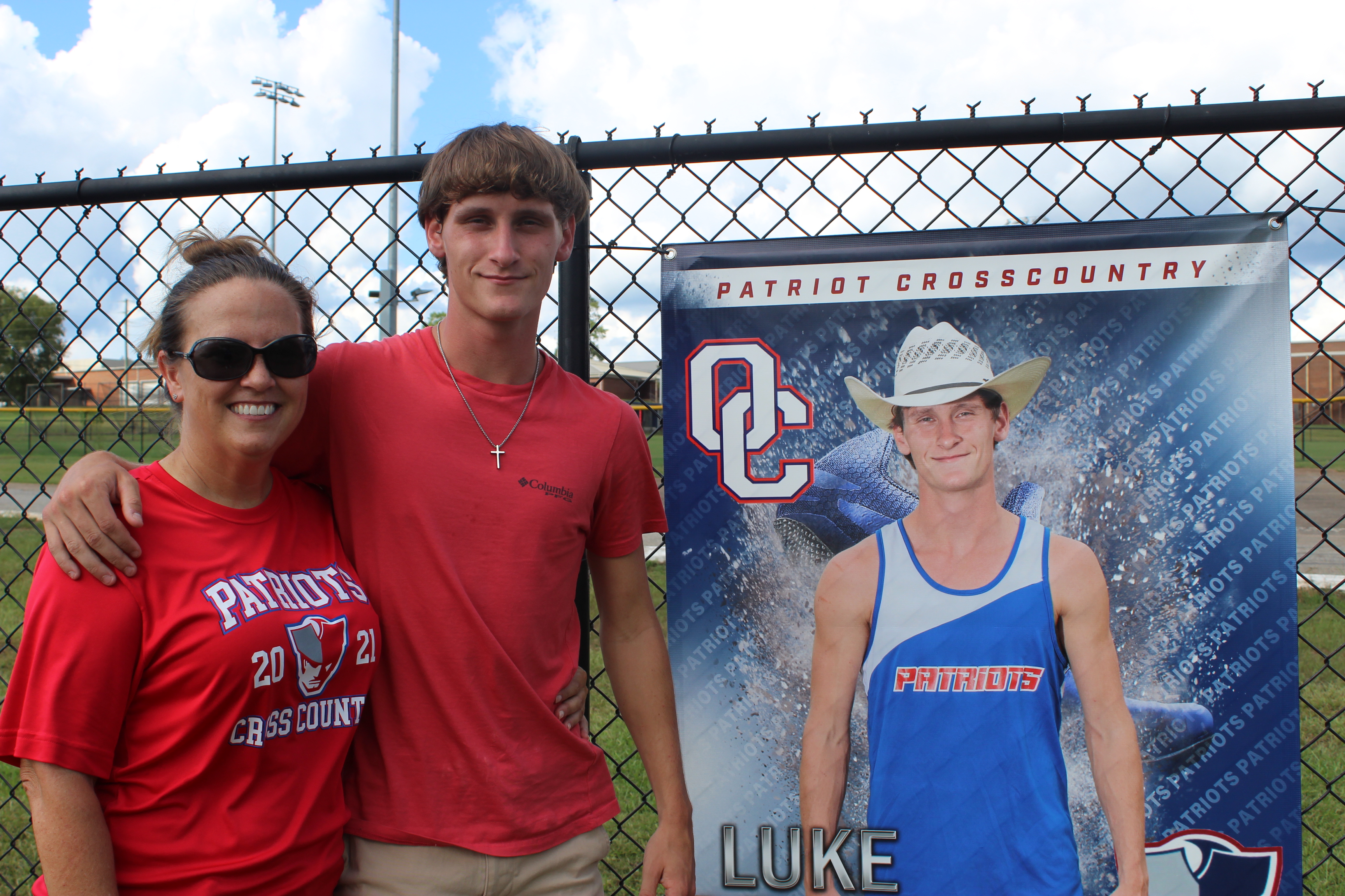 Melissa and Luke McGarity stand in front of Luke’s cross country banner at OCHS stadium after a recent cross country practice. Melissa has been Luke’s coach throughout his high school career. (Maggie Ruland/The Oglethorpe Echo)
