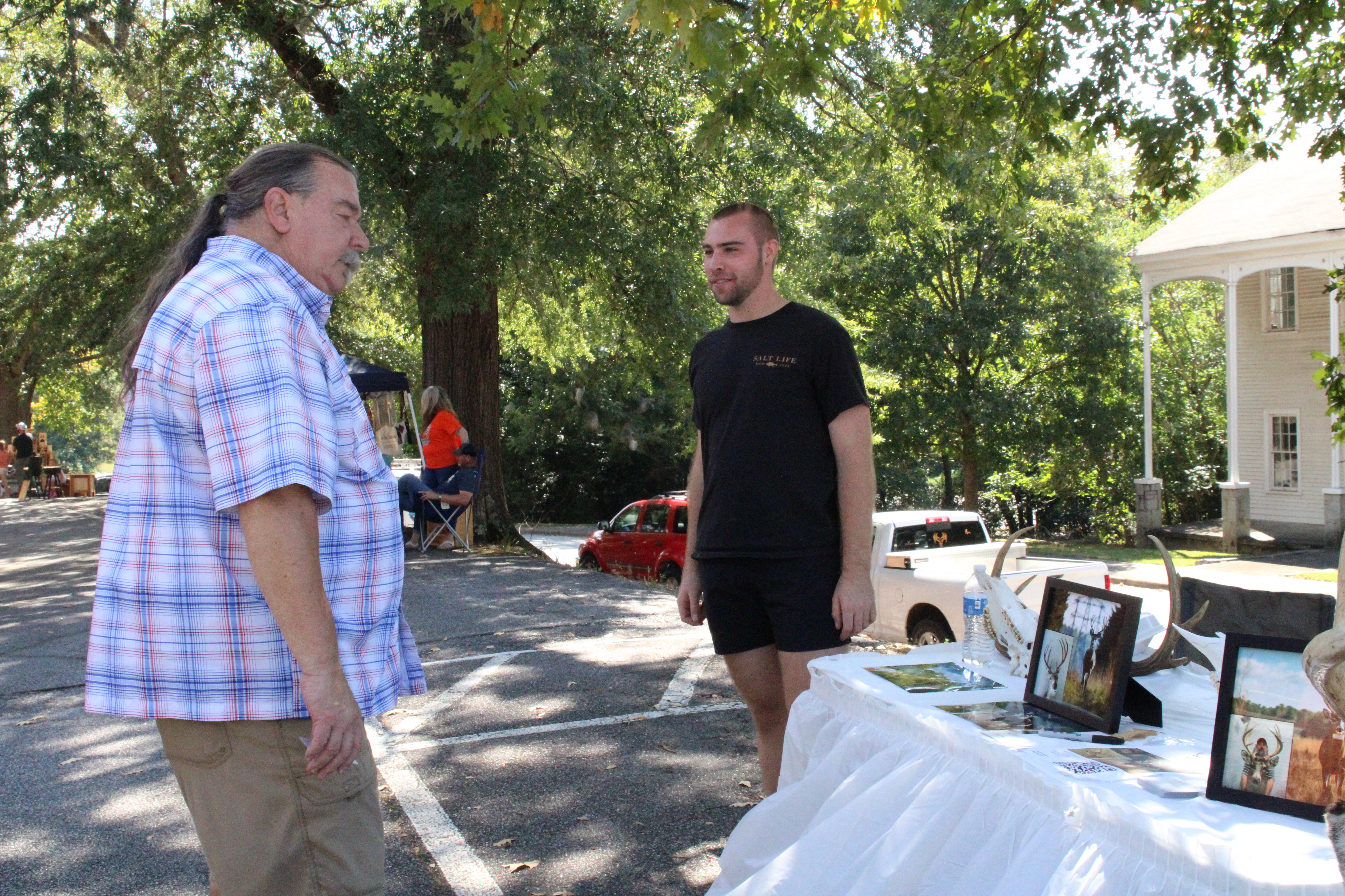 Dave Gossage (left), chairman of the Oglethorpe County Republican Party, takes a look at Colton Smith's new taxidermy buisness, called Smith Bros. e-Taxidermy. Smith uses advanced artificial intelligence prompts and Photoshop to visually recreate dead deer. (Photo/Elena Acosta)