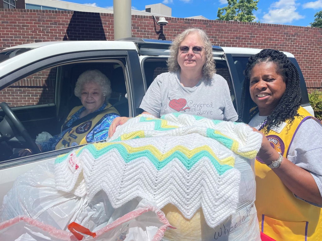 Corrine Thiel (from left), president of Oglethorpe County Lions Club, Virginia Sanders, founder of Covered with Love and Emma Walter, secretary of Oglethorpe County Lions Club display a blanket from Covered with Love to include in pajama packs. The club donates pajamas and other items to Piedmont Athens Regional for children with extended stays. (Submitted Photo).