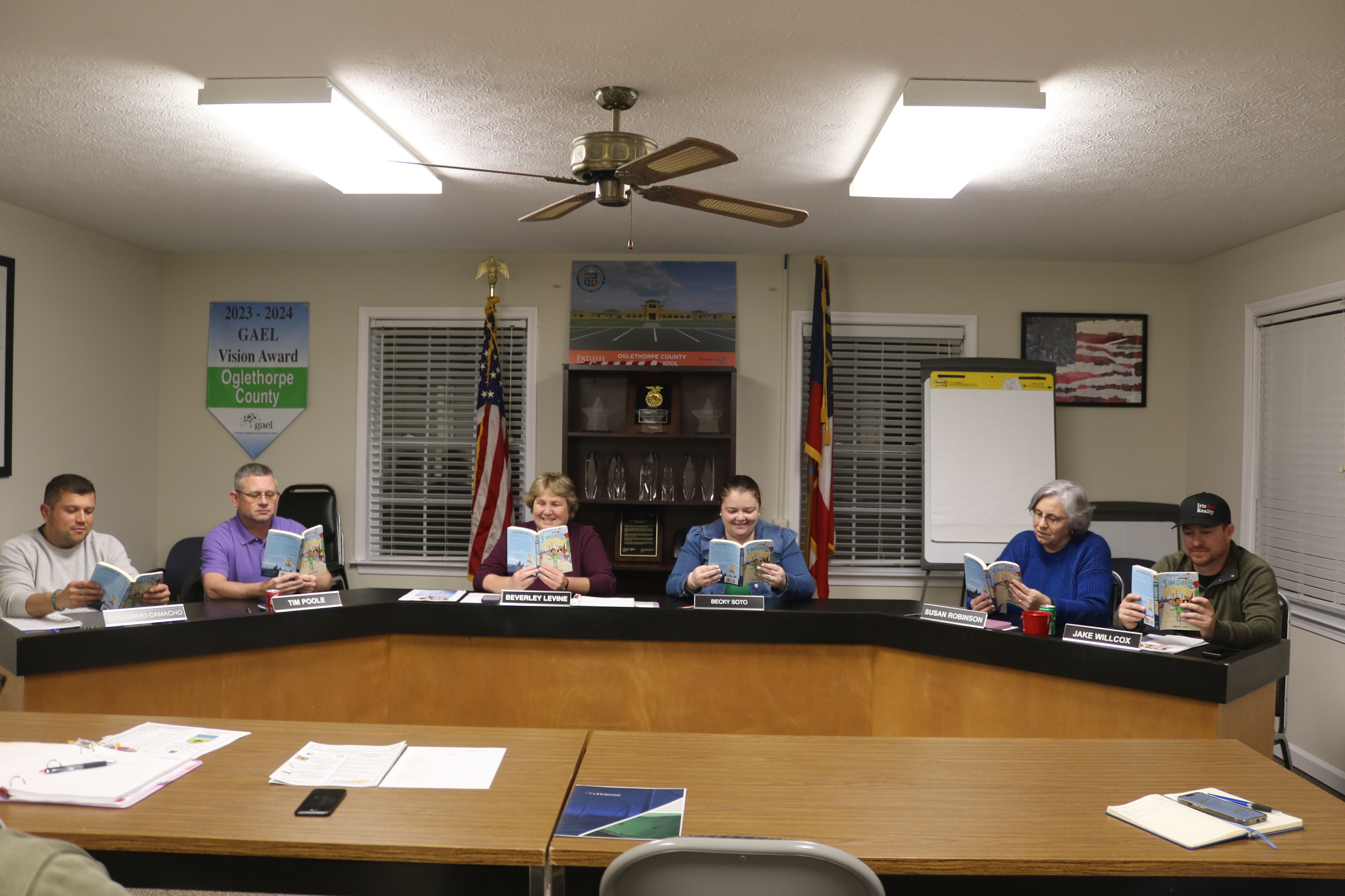The Oglethorpe County Board of Education — Guillermo Camacho (from left), Tim Poole, Beverley Levine, Becky Soto, Susan Robinson and Jake Willcox — gets into the One School One Book spirit by grabbing their copies of “Simon B. Rhymin’ ” at the meeting on Tuesday night. (Ellie Pool/The Oglethorpe Echo)