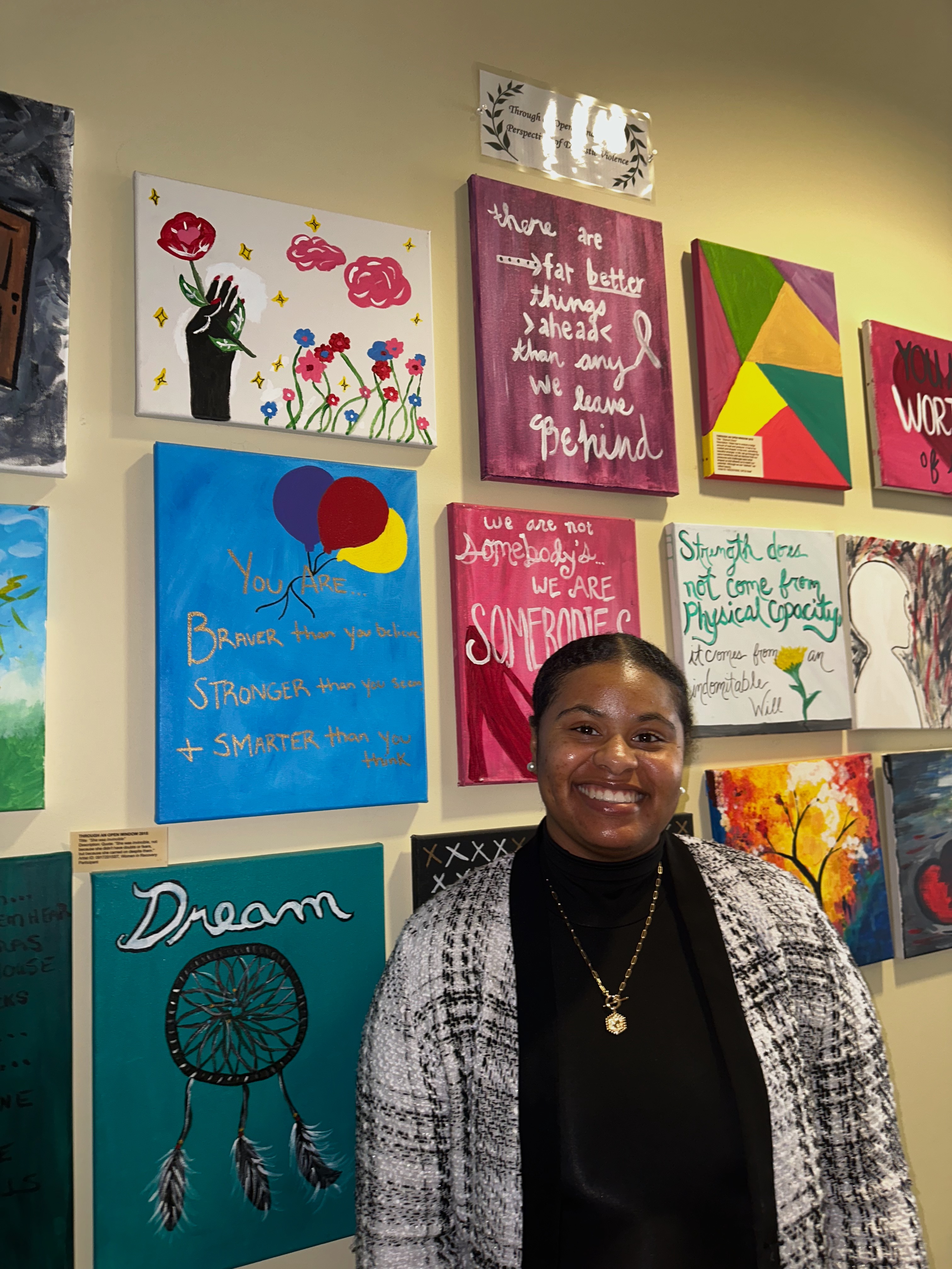 Tiara McRae, the legal advocate for Project Safe, stands in front of an art wall. The art is all created by individuals who have experienced domestic abuse and told their story at an event called Through an Open Window. (Lily Murphy/Oglethorpe Echo).