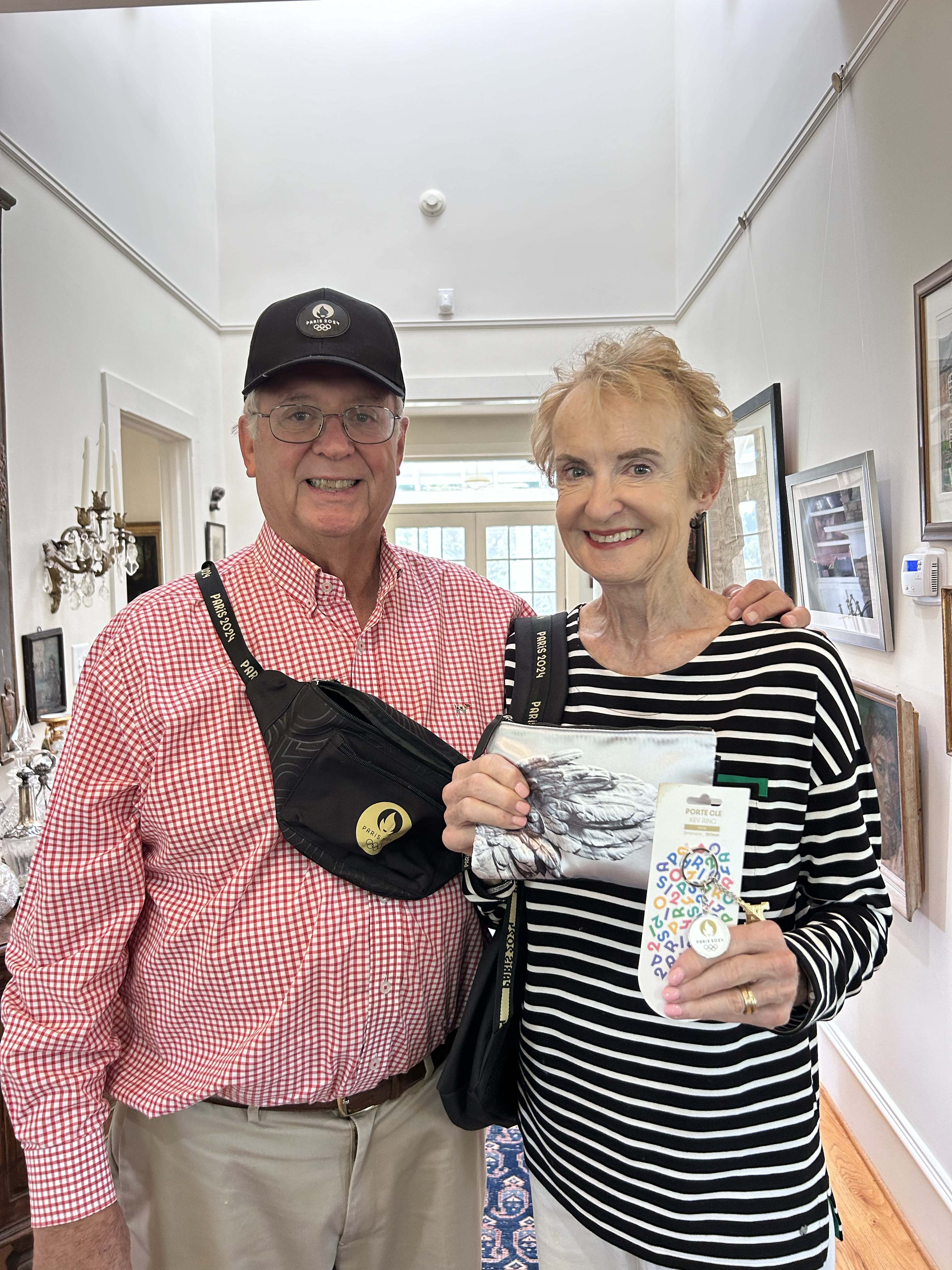 John and Jane Robertson stand in their house in Smithonia with souvenirs from their trip to Paris to see the 2024 Summer Olympics. The items include a fanny pack, backpack, hat, keychain and pouch. (McCain Bracewell/The Oglethorpe Echo)
