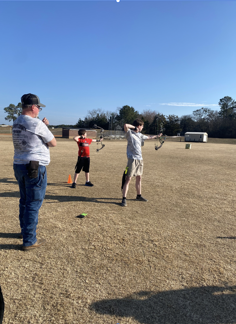 Billy Shelnutt offers advice to eighth grader Xander Bryant and fifth grader Ty Crowe at the OCMS soccer fields on Feb. 9. Bryant and Crowe are practicing for the state archery match on May 3 at the Rock Eagle 4-H Center. (Photo/Anna Izquierdo)