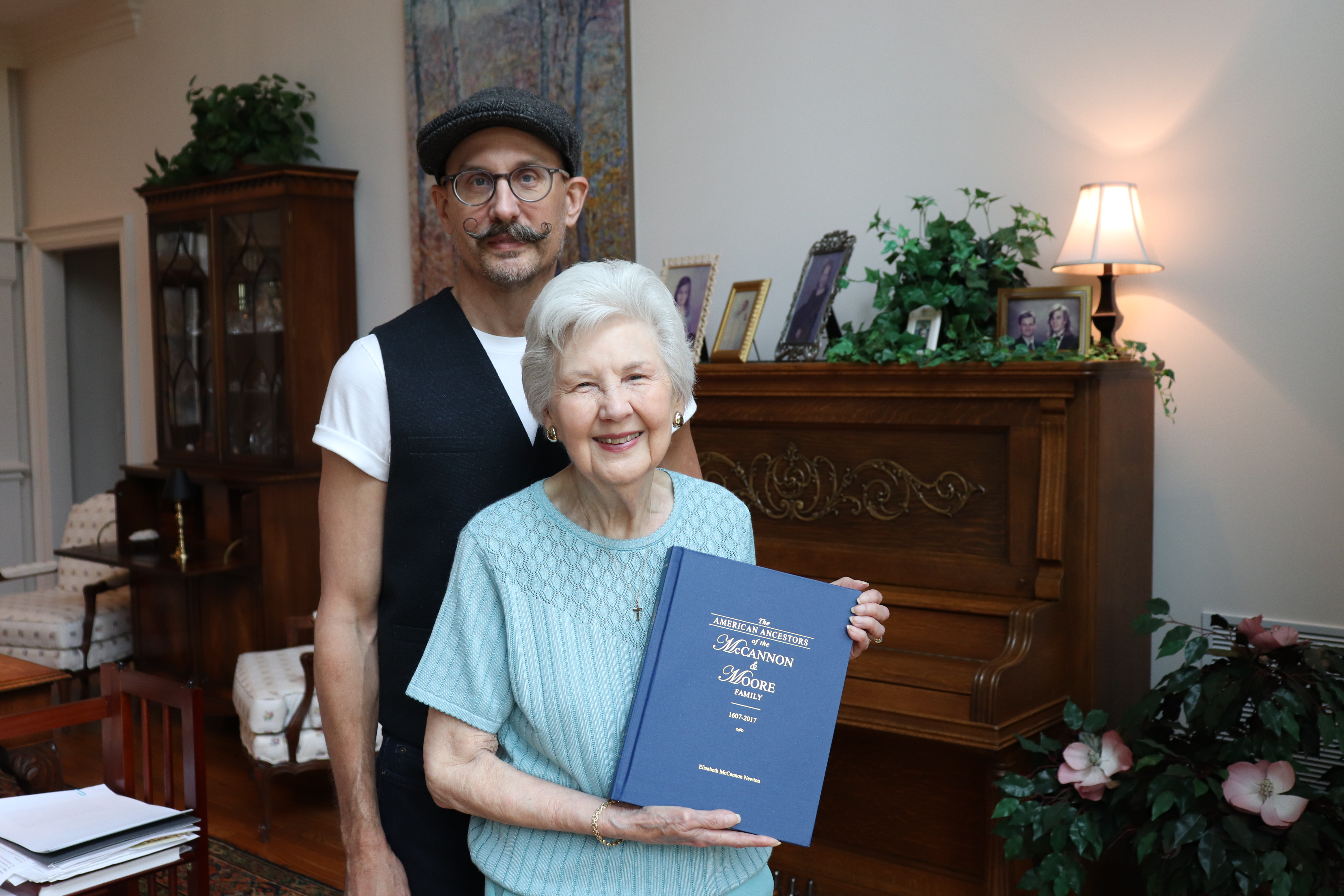 Elizabeth Newton and her son, David, pose for a portrait in Elizabeth’s Cumming residence on April 7, 2025. Elizabeth holds one of four genealogical history books she’s published, which features ancestors who will be honored at a memorial service this weekend. (Photo/Julianna Duennes Russ) 