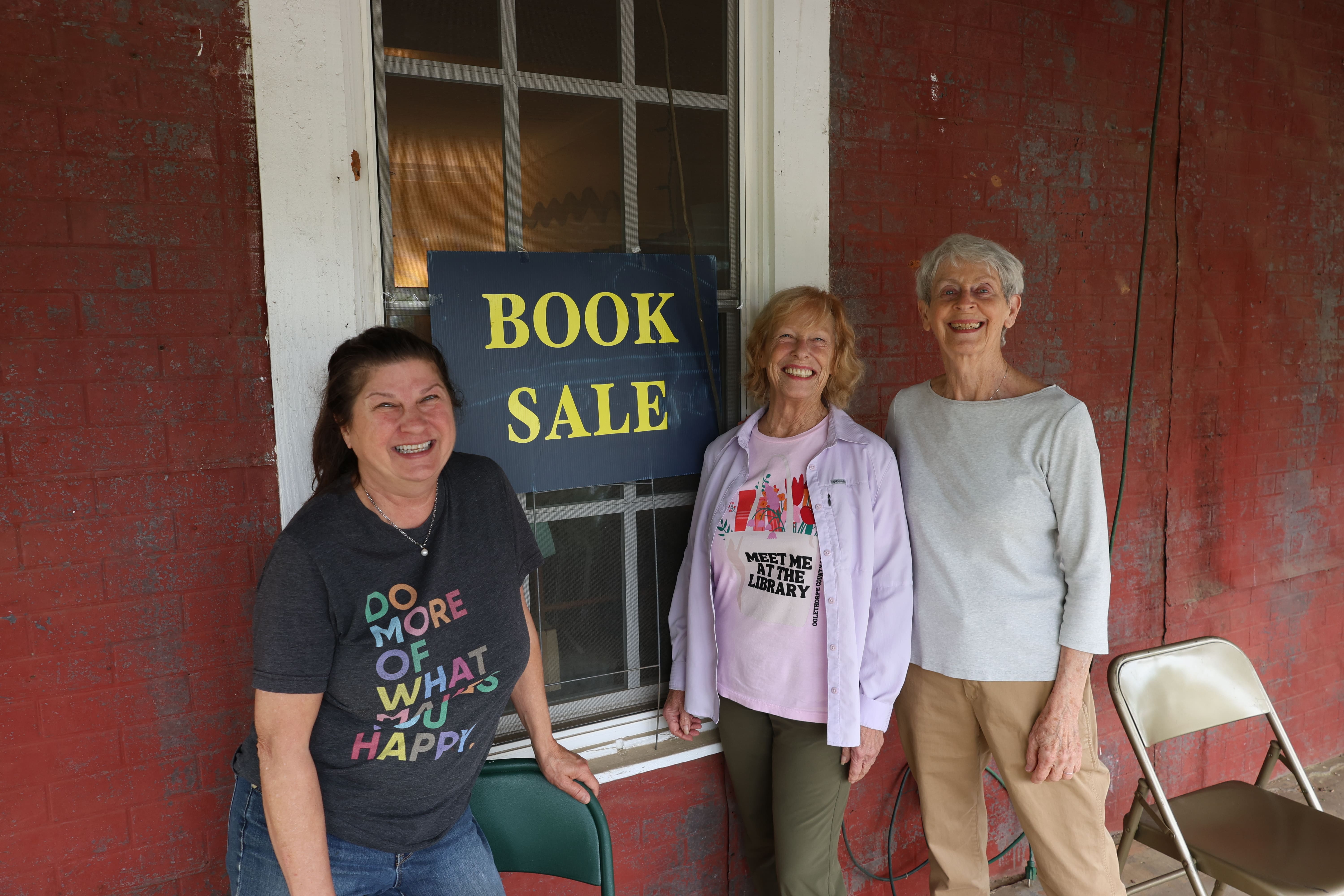 Trina Gaither of Arnoldsville (from left), Babs DeArmond of Crawford and Mary Frey of Arnoldville stand in front of the book sale sign on the porch of No. 3 Railroad St. during the fourth annual Friends of the Oglethorpe County Library Book and Art Sale last Saturday. The show will feature local artists, jewelry designers, authors and woodworkers, among others. (Photo/Olivia Wilson)