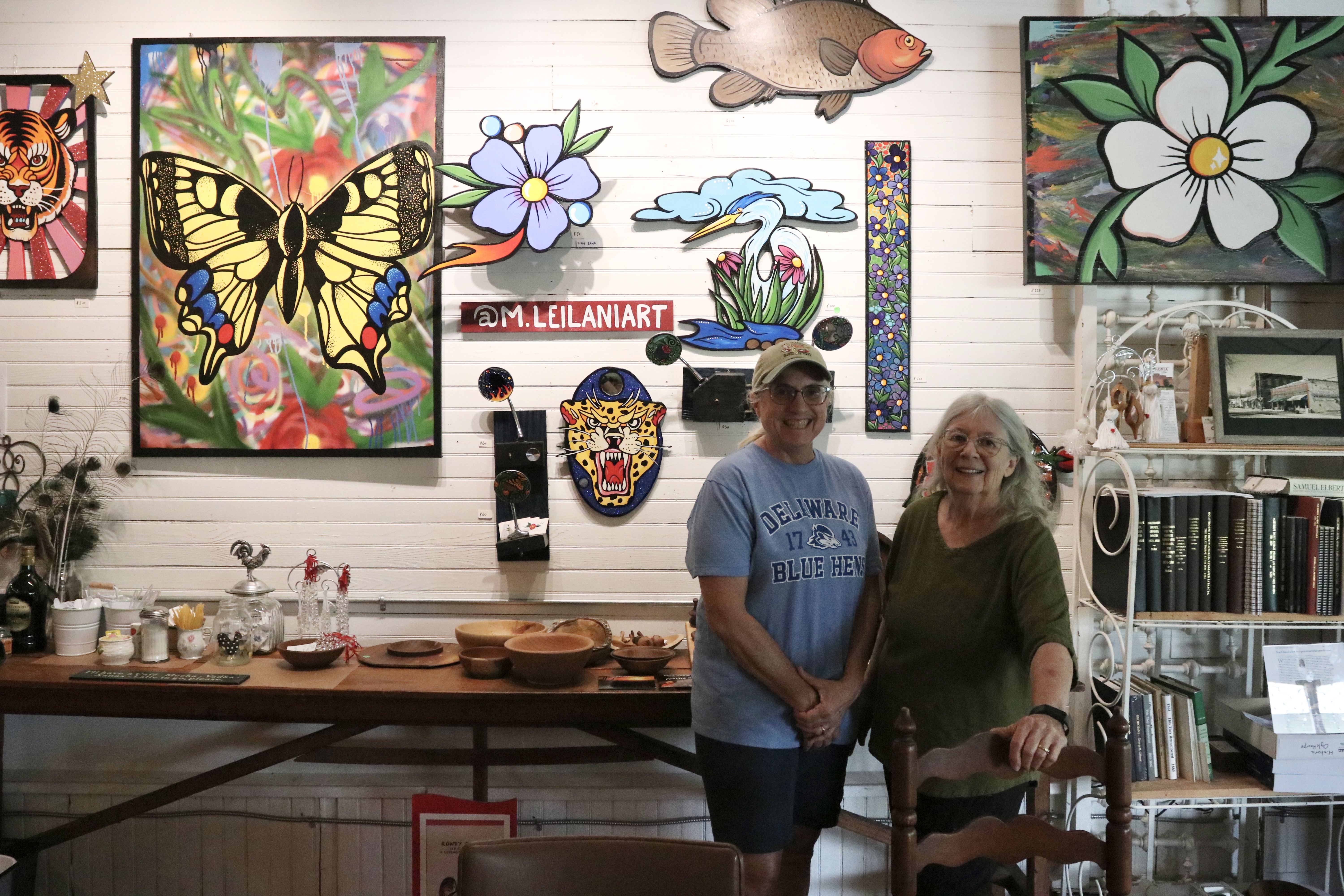 Rowdy Rooster co-owners Jamie Lewis (left) and Kathleen deMarrais stand next to Marisa Mustard’s hanging art display. The display is Mustard’s first exhibit inside the cafe. (Photo/Anna Izquierdo)