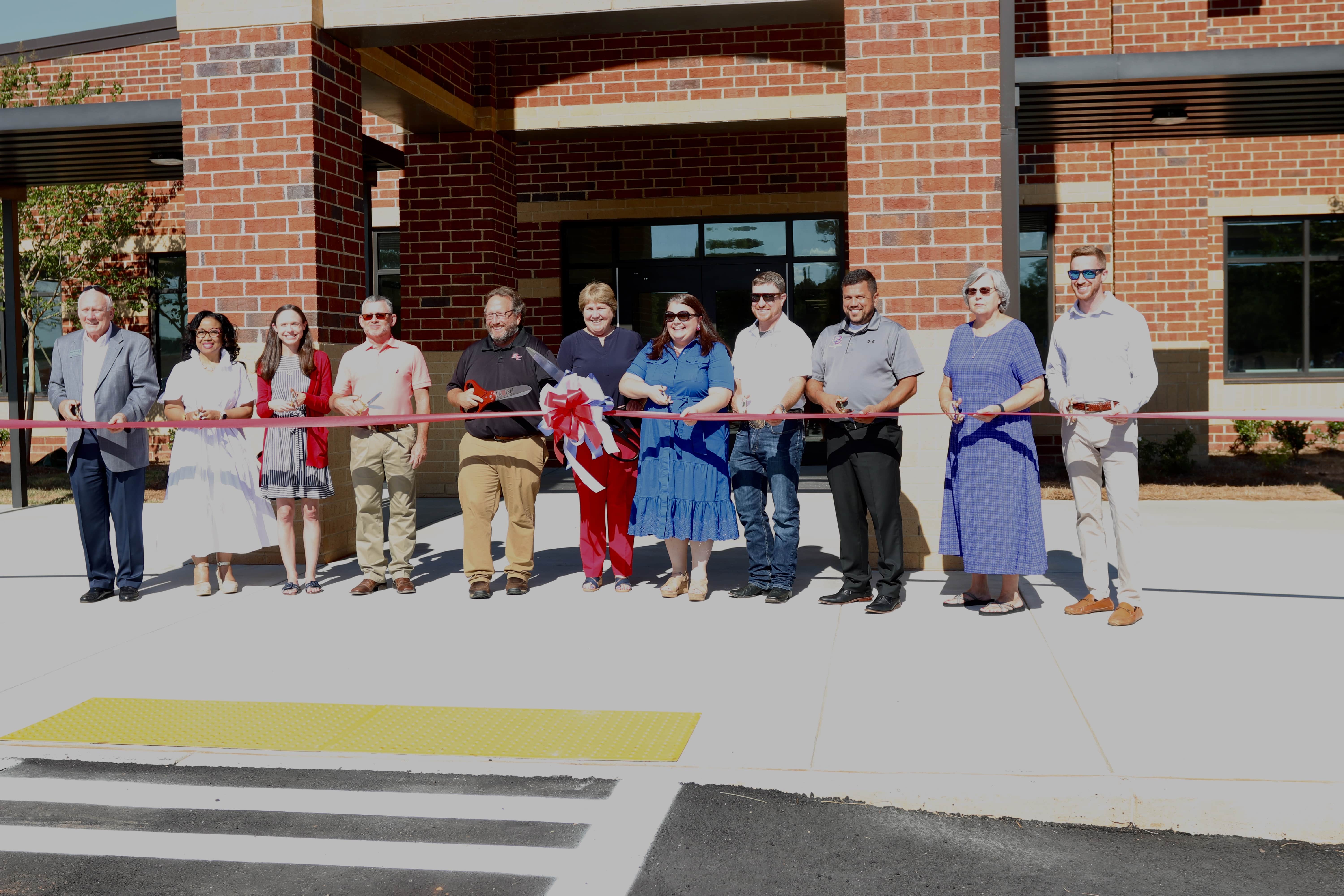 Southern A&E CEO emeritus Steve McCune, assistant superintendent Kanya Cornish, OCES principal Katie Baldwin, BOE vice-chair Tim Poole, operations director Paul Thiel, superintendent Beverley Levine, BOE chair Becky Soto, Jake Willcox, Guillermo Camacho, Susan Robinson and Parrish Construction senior project manager Alex Johnson prepare to cut the ribbon to mark the opening of the new elementary school Sunday. (Photo/Anna Izquierdo)