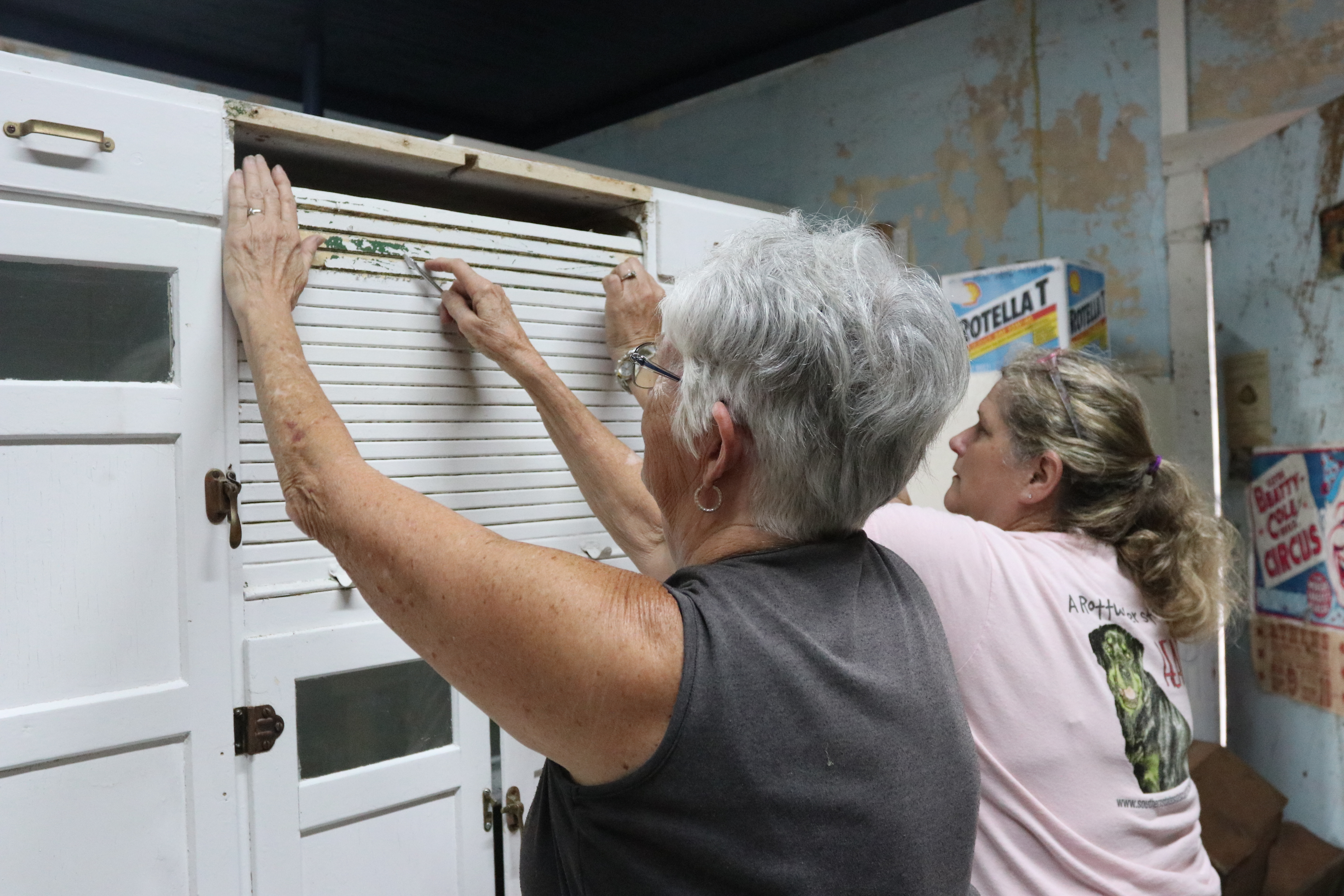 Linda Parish and Gina Holloway scrape paint off a cabinet on Aug. 22, 2025 to prepare for First Friday. The cabinet will hold drinks and food for Lexington Market Place's First Friday event on Sept. 5, 2025. (Mia Fishman/The Oglethorpe Echo) 
