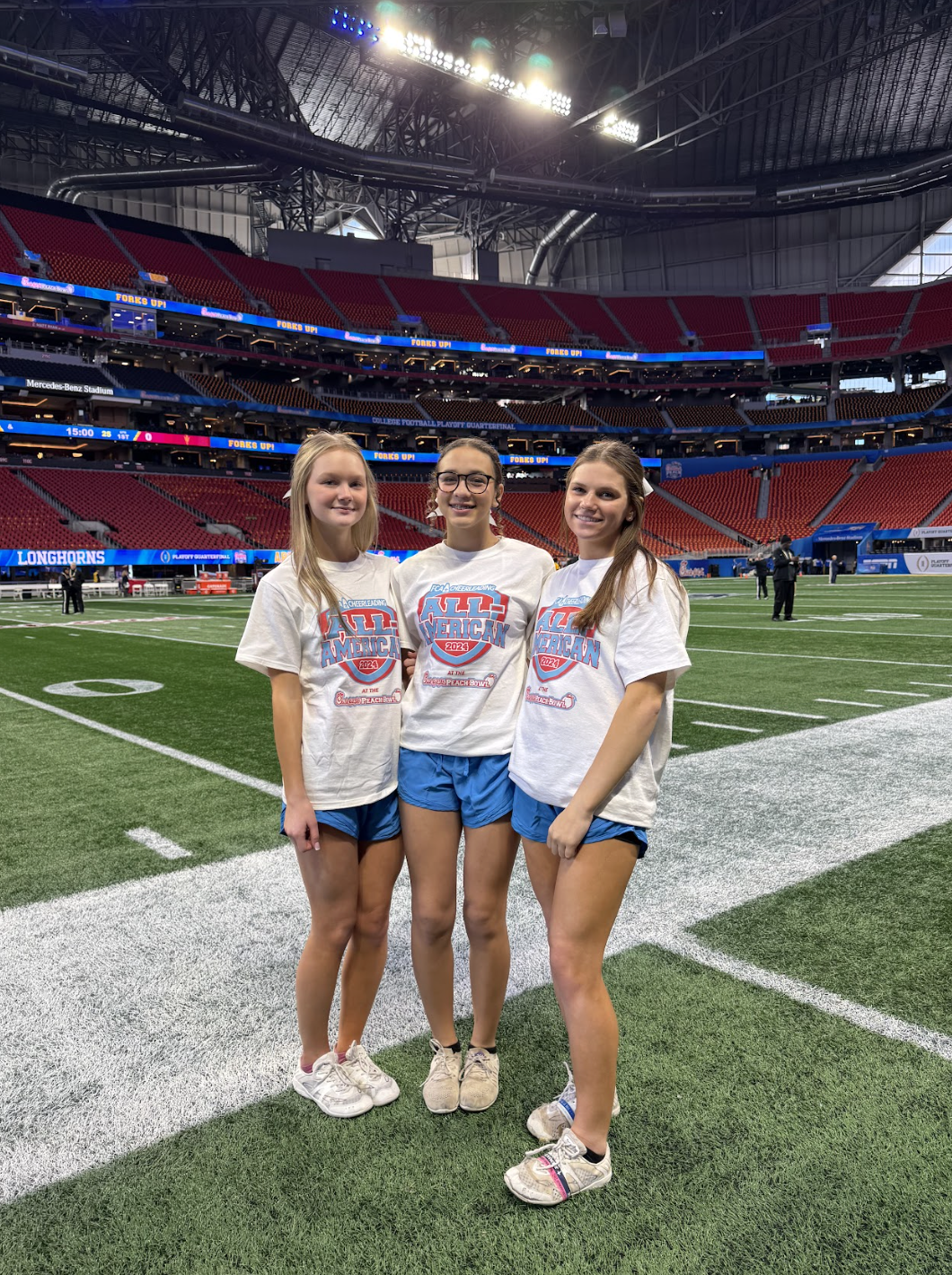 Lili Holt (from left), Abby Hormeku and Kensie Brown, Oglethorpe County’s first FCA Cheer All-Americans, smile on the Mercedes-Benz Stadium sidelines during the Chick-fil-A Peach Bowl festivities last year. Holt and Brown will return to the Peach Bowl as All-Americans next month. (Photo/Submitted)