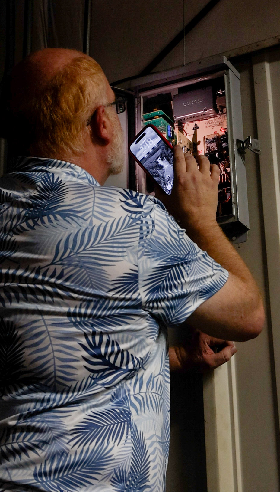 Douglas Spencer uses the flashlight on his phone to look at the  control panel of the tornado siren in the Lexington Volunteer Fire  Department. The siren’s electronics were last upgraded in 2003. (SARAH ROPER/THE OGLETHORPE ECHO)