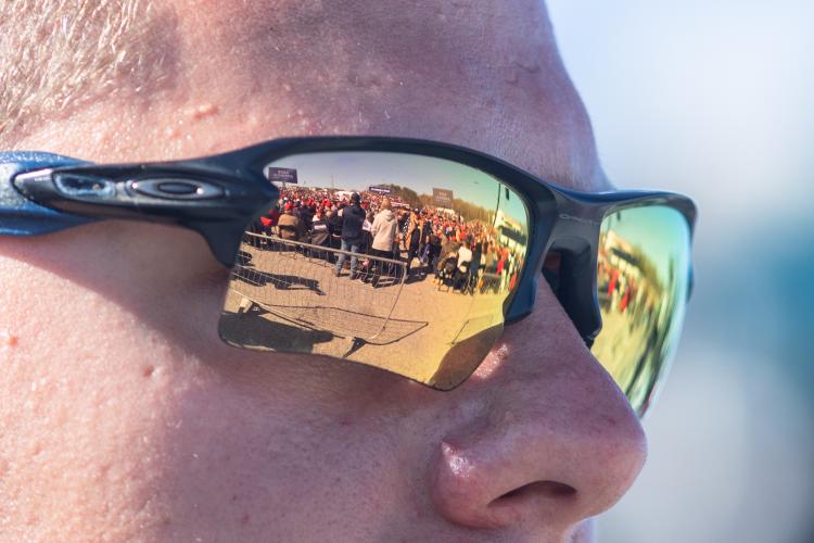 The crowd of the Save America rally reflects off an attendee’s sunglasses at the Atlanta Dragway on Saturday, March 26, 2022 in Commerce, Georgia. Initial estimates anticipated close to twenty thousand attendees, but the crowd ended up being closer to five thousand. The area reflected in the sunglasses was not open to the majority of the crowd. Most attendees crowded into two areas behind the seated crowd and adjacent to the media risers. The area behind was mostly empty. (Julian Alexander/For The Echo)