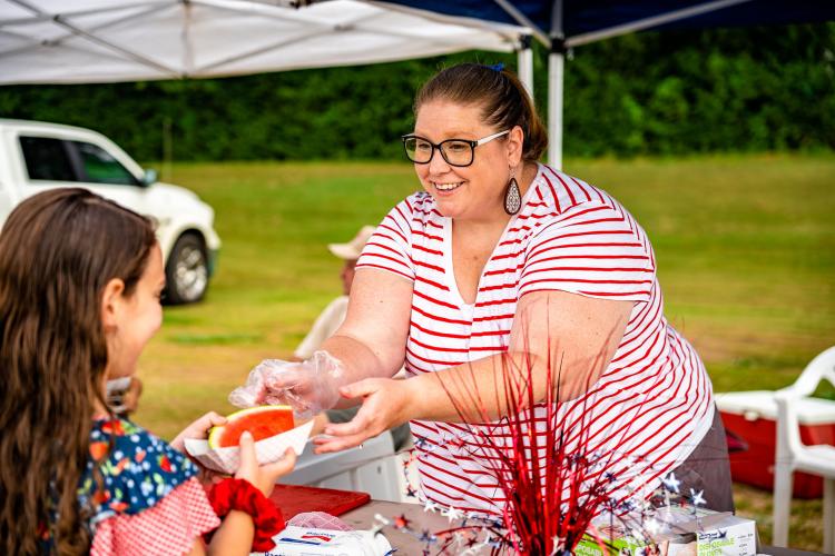 Crawford’s Heather Stevens hands out watermelon while manning the Crawford Baptist Church’s table at the Fourth Annual Independence Day Celebration at Bryan Park on Monday. (Photo/Jack Casey)