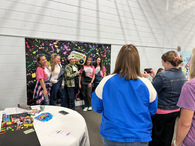 Oglethorpe County teachers dressed in colorful ’90s fashion take a group photo at the professional learning event on Oct. 7. The event took place in the Oglethorpe County Elementary School gym, which was decorated for the event. (Photo/Megan Fitzgerald)