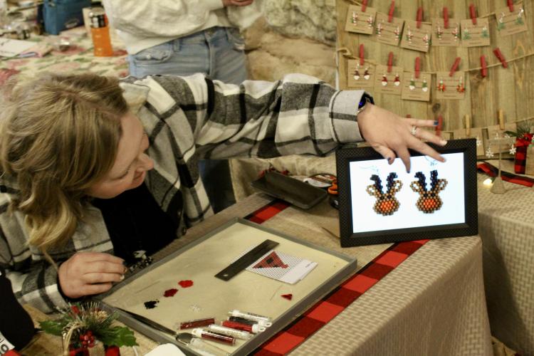 Jewelry maker Kristie Hall follows a digital pattern she created to make a pair of holiday-themed earrings. Hall crafted her jewelry at her booth so her customers could see her handiwork. (Lily Baldwin/The Oglethorpe Echo)
