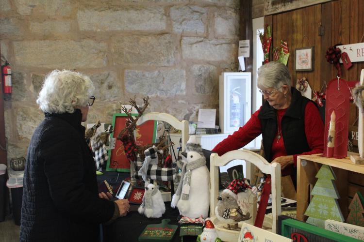 Peg Thon purchases holiday decor from Linda Parish, owner of Local Color in Lexington. Along with selling her own creations, Parish also organizes the Christmas Marketplace every year. (Lily Baldwin/The Oglethorpe Echo)