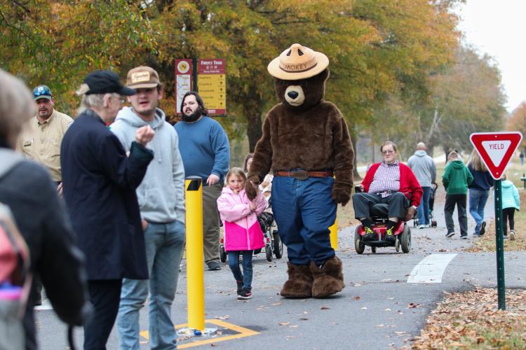 Willow Paulk (5) holds the hand of Smokey Bear, the famous forestry mascot, on their way to the  Christmas Market after riding in the Maxeys Christmas Parade.