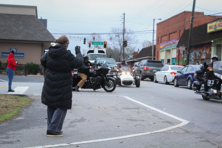 A small crowd of people waves to those driving in the War Room Show's community Christmas parade in Crawford, Georgia on Saturday, December 10, 2022. (Photo/ Basil Terhune