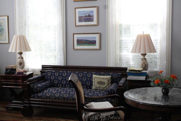 In deMarrais’s parlor, a faux-granite paint finish is visible on the tabletop decorated with flowers. This pop of vermillion flora and a Victorian armchair cast warmth into the blue room on Oct. 4, 2022. (Photo/Sarah Donehoo)