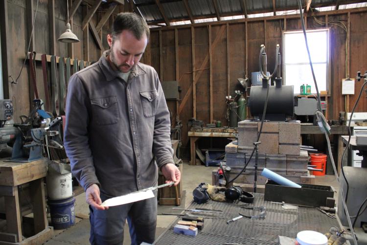 Luke Snyder holds an unfinished chef knife featuring a single bevel at Bloodroot Blades in Arnoldsville. There’s a 52-month waiting list for the knives handcrafted by Snyder and partners Katy and David Van Wyk. (Sarah Donehoo/The Oglethorpe Echo)