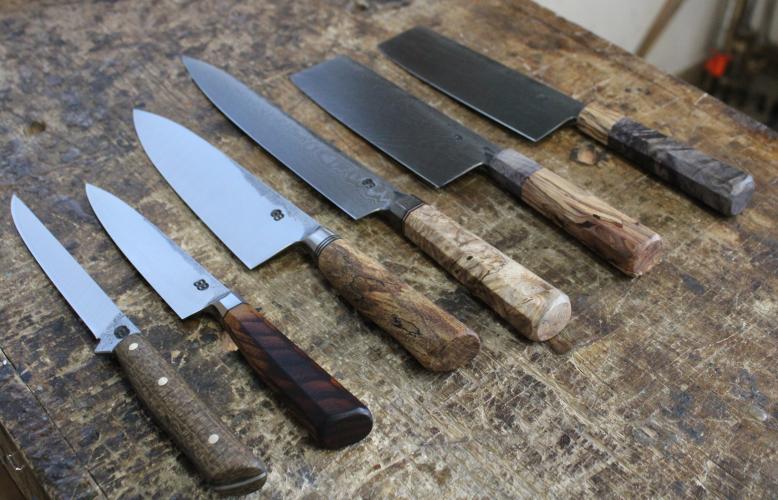 Finished knives from left to right on Feb. 13, 2023:  1. Boning knife with coffeebag laminate handle from burlap coffee sacks supplied by Charlie Mustard at Jittery Joe's in Athens and steel from a sawblade sourced from a granite mill in Elberton, Ga. 2. Octagonal integral petty knife with a scorched osage orange handle and roller bearing steel. 3. Integral chef's knife with a spalted copper beech handle and roller bearing steel from a machine shop in Birmingham, Alabama. 4. Octagonal integral Damascus slic