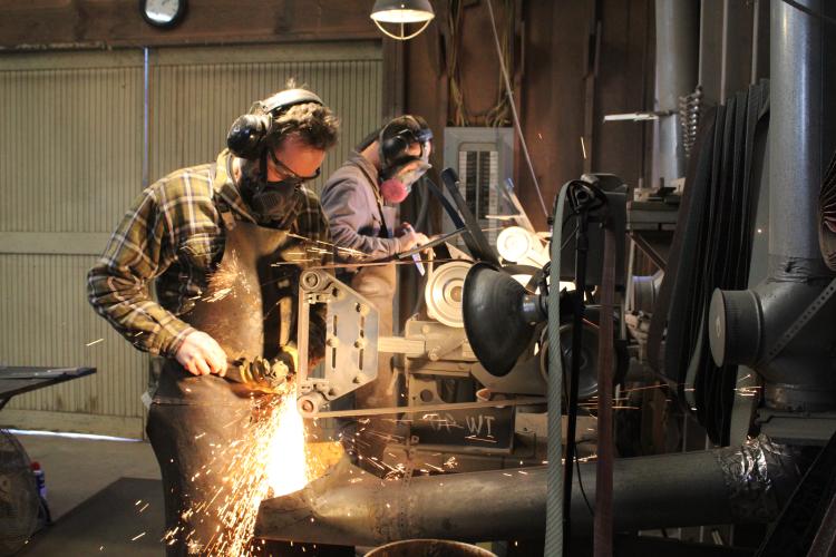 David Van Wyk and Luke Snyder belt-sanding two unfinished blades on Feb. 13, 2023. (Photo/Sarah Donehoo)