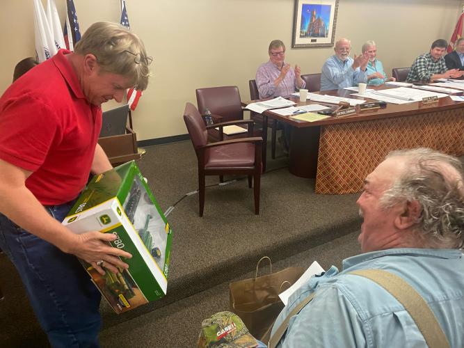 Commission Chairman Jay Paul presents former county commissioner Phil Sanders with a toy John Deere combine at this month’s commission meeting on Monday. (Dink Nesmith/The Oglethorpe Echo)
