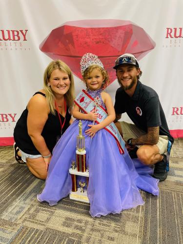 Isabella Raines, who is 5 years old, smiles with her mom, Megan Raines, and dad, Ian Willoughby, at the 2022 Ruby Elite Wonderland State pageant. (SUBMITTED PHOTO)
