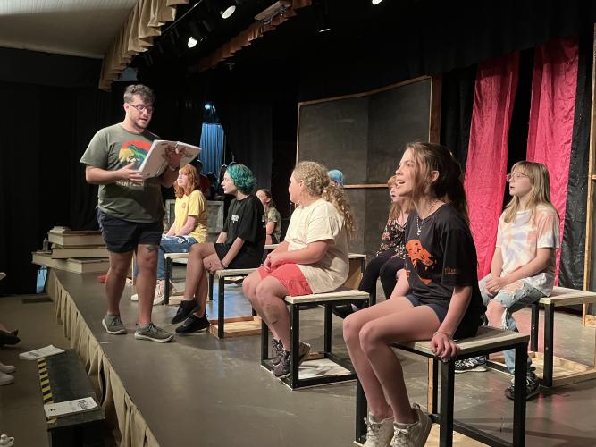 Music director Chase Cooper leads the cast of Matilda the Musical during a rehearsal on June 10 at the Historic Crawford School. Left to right are Ellie Roman, Hazel Hogan, Allie Spurlin, Thalia Smoot and Kassie Mathews; obscured are Jenna Grace Burt, Clover McGovern and Sophia Priest. Arts!Oglethorpe director Bly Hartley said the production’s actors have a wide range of ages, and the show is family-friendly. (JESSE WOOD/THE OGLETHORPE ECHO)