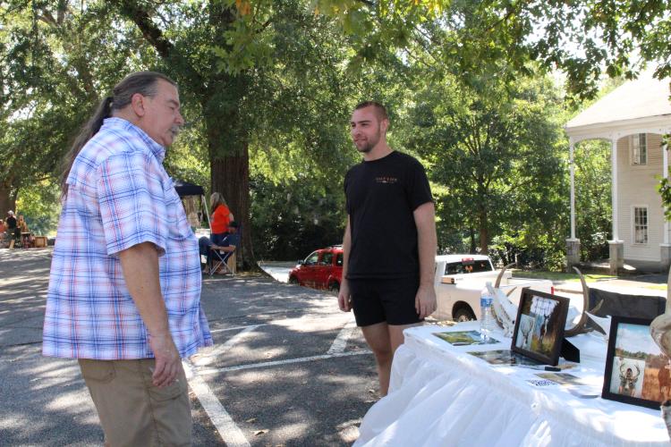 Dave Gossage (left), chairman of the Oglethorpe County Republican Party, takes a look at Colton Smith's new taxidermy buisness, called Smith Bros. e-Taxidermy. Smith uses advanced artificial intelligence prompts and Photoshop to visually recreate dead deer. (Photo/Elena Acosta)