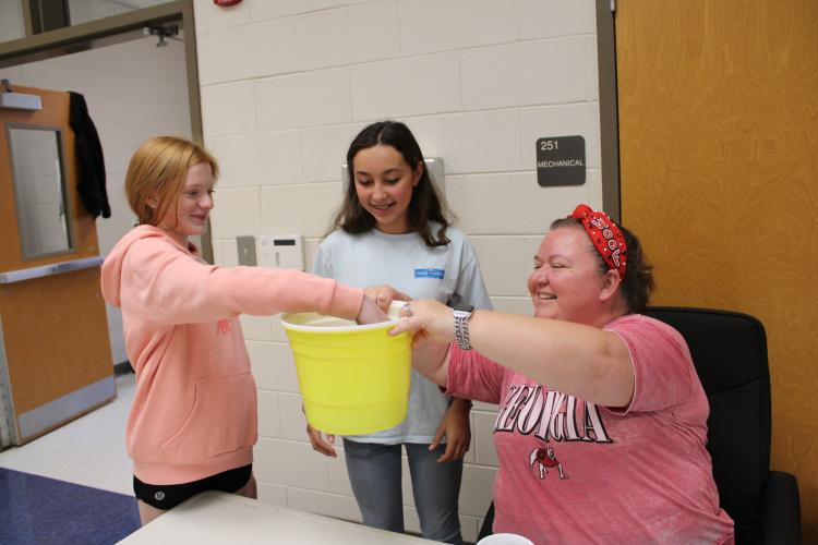 Seventh graders, Mae Matthews (left) and Izzabella Buck drew from Robyn Benton’s bucket of names to determine the seventh grade winners of the twin day contest. “It's really fun, we get to dress up without it being costumes. And it helps everyone because the more fun you put in it, the more they’ll participate and it teaches them not to do drugs,” said Buck. (Photo/Caleb Baldwin)