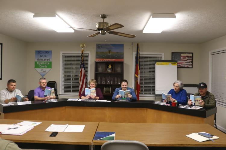 The Oglethorpe County Board of Education — Guillermo Camacho (from left), Tim Poole, Beverley Levine, Becky Soto, Susan Robinson and Jake Willcox — gets into the One School One Book spirit by grabbing their copies of “Simon B. Rhymin’ ” at the meeting on Tuesday night. (Ellie Pool/The Oglethorpe Echo)