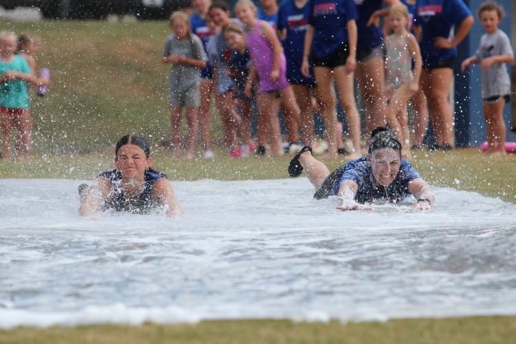 OCHS sophomore Khloe Eidson (left) and OCHS softball coach Brianna Dickens slide at the request of the campers at the end of the softball and baseball camps at OCHS last week. The coaches set up makeshift slip-n-slides for fun and help beat the heat. (Torin Smith/The Oglethorpe Echo)