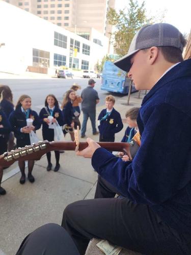 Fellow FFA Convention attendees gather as Hunter Boswell plays and sings on a street in Indianapolis. Boswell has been performing since he was 9, and can play the bass guitar, piano, acoustic guitar and drums. (McCain Bracewell/The Oglethorpe Echo)