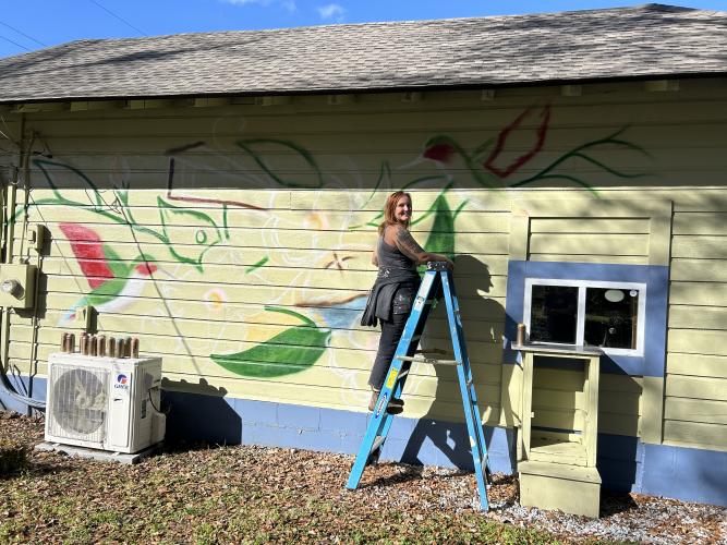 Marisa Mustard, who is from Athens, works on the outline of her mural on the side of the Rowdy Rooster in Lexington. The painting on the deli/bakery is now complete. (Submitted Photo)