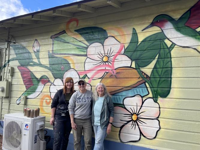 Artist Marisa Mustard (left) stands with Rowdy Rooster co-owners Jamie Lewis and Kathleen deMarrais in front of the new mural. Mustard has painted murals in several cities. (Dakota Meeks/The Oglethorpe Echo)