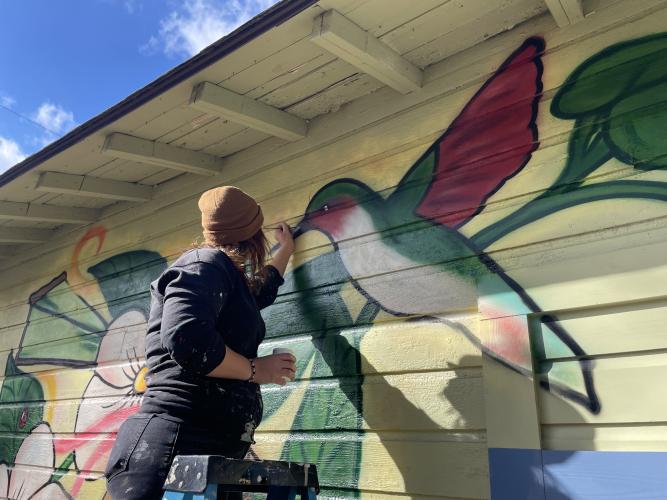 Artist Marisa Mustard adds the finishing touches to the mural that she painted on the side of Rowdy Rooster in Lexington. The mural includes pies, moon flowers, hummingbirds and a ladybug. (Dakota Meeks/The Oglethorpe Echo)