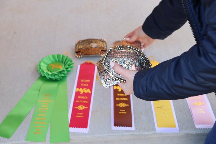 Oglethorpe County High School senior Raegan Poulnott receives a ribbon or belt buckle when she places in a livestock competition. She lines up her ribbons from her most recent competition, where she placed sixth overall in Senior Showman at the NJSA Winter National Swine Show on Jan. 15, 2025. (Photo/Lilly Stone)
