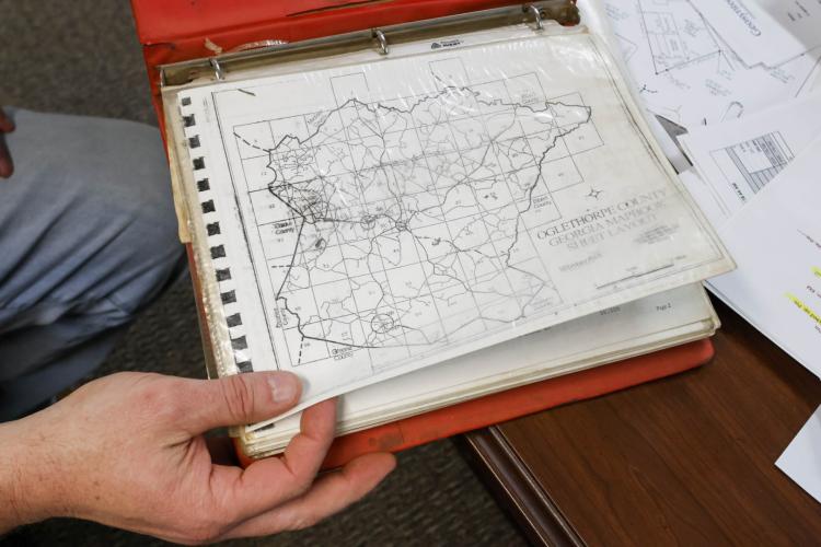 A close-up shot of a collection of maps of roads within Oglethorpe County, held by Public Works Director Adam Nation within the Board of Commissioners Office in Oglethorpe County on Monday, Feb. 5, 2025. Across the roughly 250 miles of dirt public roads and 250 miles of paved public roads throughout the county, Nation claims Oglethorpe County has some of the best. “We’re proud of the shape our roads are in.” (Photo/Felix Scheyer)