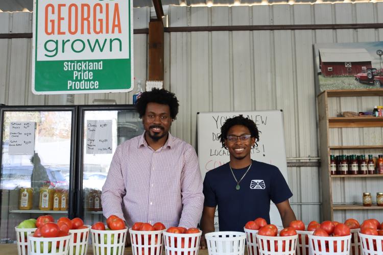 Kendall Strickland, owner and founder of Strickland Pride Produce, and new employee Xavier Sapp pose for a photo behind the store's counter at the February Fling event on Feb. 7, 2025. Customers came out to support Strickland Pride's first year in its storefront location and nearly five years in business overall. To keep up with the increase in business at the new location, Sapp joined Strickland's team about six months ago to assist with daily storefront operations. (Photo / Lilly Stone)