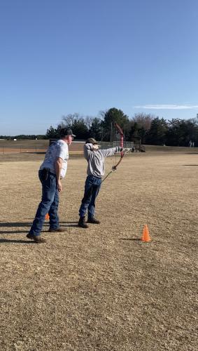 Billy Shelnutt coaches eleventh grader Grace Foland on Feb. 9 at the OCMS soccer field, Foland is practicing for the state archery match on May 3 at the Rock Eagle 4-H Center. (Photo/Anna Izquierdo)