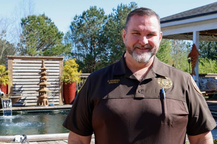 Sheriff David Gabriel poses for a portrait in front of the upper koi pond with his backyard on Monday, March 17, 2025. Even as a child, Gabriel had a love of observing fish and wildlife. “We had a creek we’d stop up, dam the creek up. We’d get brim and catfish and stuff and put it in the creek, you know, and then a storm would come through and blow the dam out, and that would be that,” Gabriel said. (Photo/Felix Scheyer)