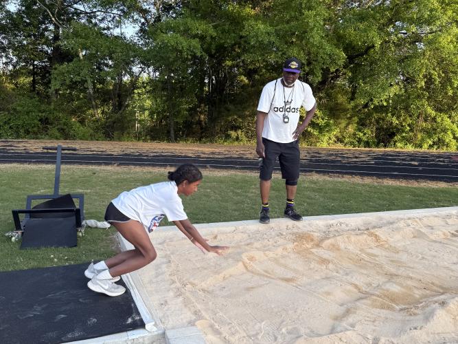 Brielle Jones bends her knees in preparation to jump into the standing jump pit as Dwight Howard Sr. watches on April 17. Jones won the fourth heat of the girl’s standing long jump event at the North Georgia Youth Track and Field Championship on April 19. (Photo/Anna Izquierdo)