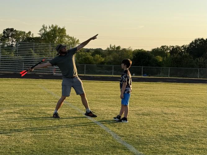 Javelin coach Craig Cheesborough demonstrates javelin form to Harrison Ditty, 9, on April 17. Cheesborough advised athletes to open their chests and keep their “eyes in the sky” when preparing to throw. (Photo/Anna Izquierdo)