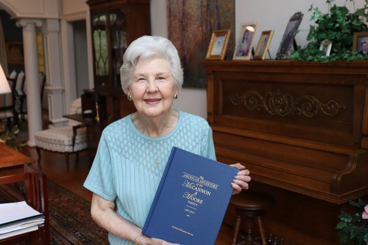 Elizabeth Newton, a librarian and genealogy enthusiast, poses with a book she published on her family's history in her Cumming residence on April 7, 2025. “They're living people to me," Newton said. "They're not just a name." (Photo/Julianna Duennes Russ)