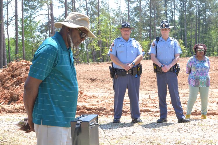 Dwight Howard, founder of the Holy Ground Community Garden, bows his head in front of the Georgia State Patrol’s Sgt. Neil Frankel (left) and Trooper Tyler Crowe and State Rep. Kim Schofield (D-Atlanta). They were listening to the garden's theme song by Jackie Howard, Howard's sister, at the grand opening. (Photo/Adriana Cascio)