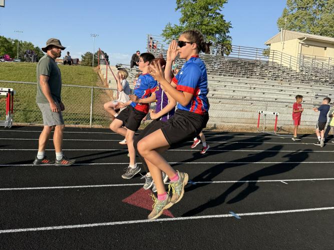 Meara Shaw, 9, pumps her arms and brings her knees to her chest during track and field warm ups on April 17. Craig Cheesborough advised athletes to “keep (their) arms bent” while completing stretches. (Photo/Anna Izquierdo)