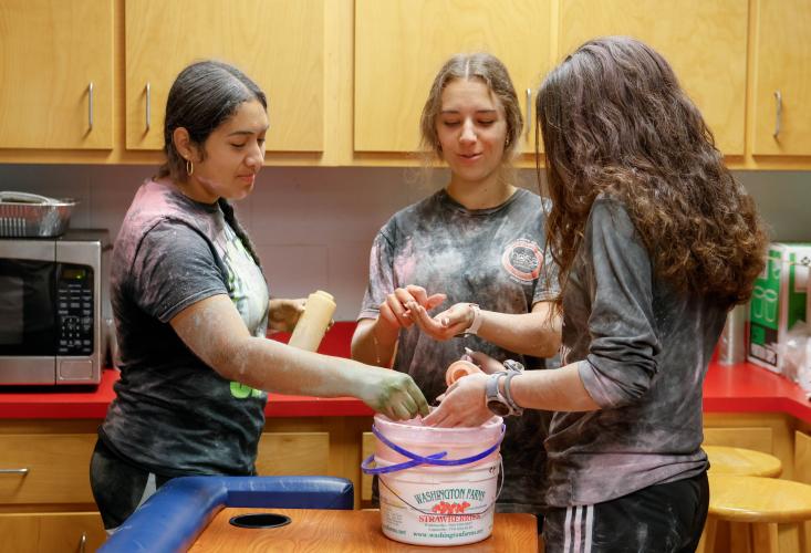 Genesis Palma Umana (left), Madeline Forschler (center), and Harper Palmer (right), all senior students at Oglethorpe County High School, work together to clean the buckets used to hold the colorful chalk throw during the Oglethorpe County High School Color Run within the Oglethorpe County High School gym in Oglethorpe County, Georgia, on Saturday, April 26, 2025. “Even though a lot of these a lot of these folks are friends, some of them are in different grades, some of them do completely different activiti
