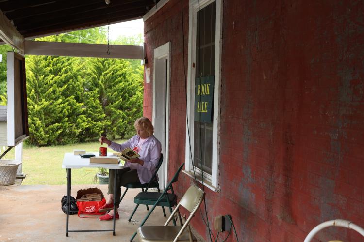 Babs DeArmond of Crawford sits on the porch of No. 3 Railroad St. reading during the book sale on Saturday, May 3. Babs is currently serving as the vice president of the Friends of the Oglethorpe County Library. (Photo/Olivia Wilson)